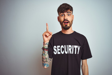 Young safeguard man with tattoo wering security uniform over isolated white background pointing...