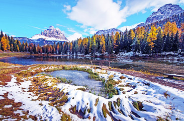 The charming landscape with frozen snowy pond and wooden bridge on a background of Tre Cime de Lavaredo mountains on the Antorno Lake, Dolomites Alps. (Meditation, anti-stress, relaxation - concept)