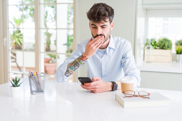 Young business man using smartphone sending a message cover mouth with hand shocked with shame for mistake, expression of fear, scared in silence, secret concept