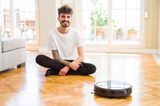 Young man using automatic vacuum cleaner to clean the floor, controling machine housework robot