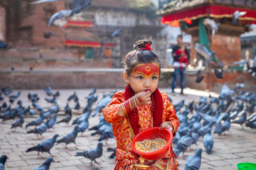 Little girl dressed as Kumari God feeding the pigeons at Kathmandu Durbar Square during Indra Jatra...