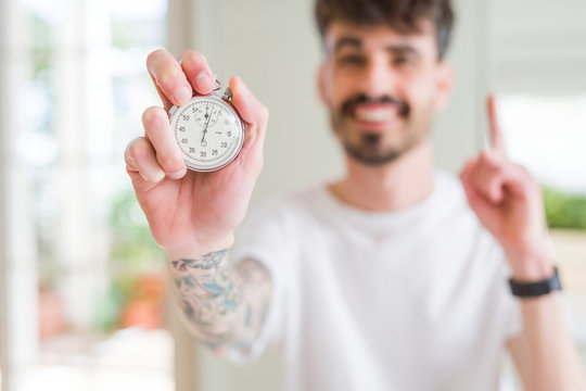 Young man using holding stopwatch surprised with an idea or question pointing finger with happy face, number one