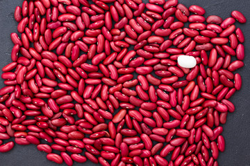 Red beans on a black background, one white bean in the corner of the picture, top view