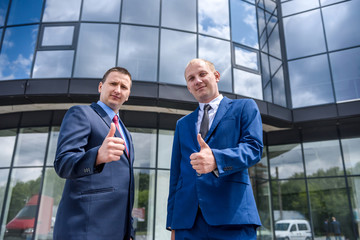 Two men in suits showing thumbs up outdoors