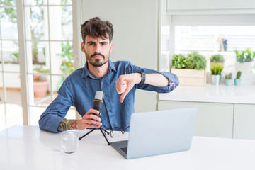Young man recording podcast using microphone and laptop with angry face, negative sign showing...