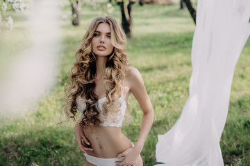 Naklejka premium beautiful sexy blonde girl posing in white lace underwear in the garden