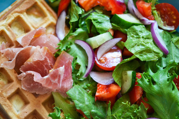 Belgian waffles with prosciutto and vegetable salad on the kitchen table.