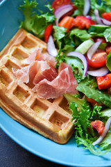 Belgian waffles with prosciutto and vegetable salad on the kitchen table.