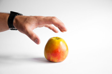 An apple stands on a white table on a white background. Hand takes apple