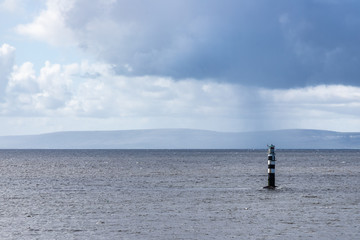 Lighthouse in Galway bay with rainy cloud and burren mountains in background