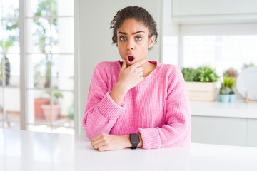 Fototapeta na wymiar Beautiful african american woman with afro hair wearing casual pink sweater Looking fascinated with disbelief, surprise and amazed expression with hands on chin