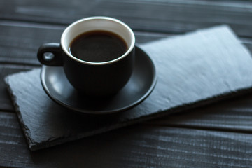 Espresso coffee in a small black cup on a stone stand on a black wooden table, selective focus