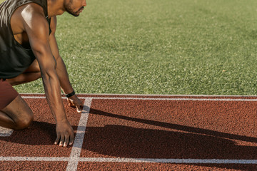 Side view cropped shot of sprinter about to start a race at stadium with sun shadow