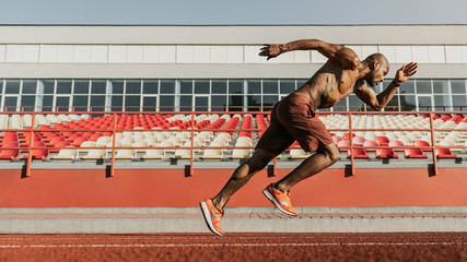 Side view shot of male sprinter running on the sport track. Athlete runner doing workout at the stadium - obrazy, fototapety, plakaty