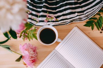 Cup of coffee and flowers on wooden table with notebook and striped fabric