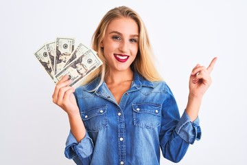 Young beautiful blond woman holding dollars standing over isolated white background very happy pointing with hand and finger to the side