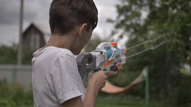 happy boy shoots a water pistol outdoors in the village