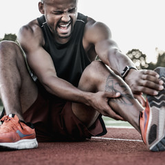 Tired sportsman suffering from knee pain at the stadium track