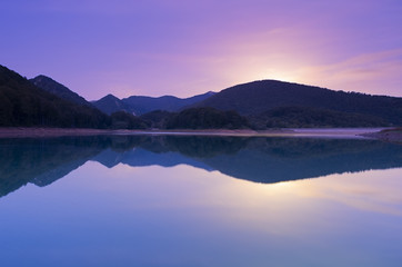 Fototapeta na wymiar Full moon rise at dusk in the Lareo reservoir, Aralar mountain range, Euskadi
