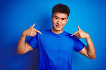 Young asian chinese man wearing t-shirt standing over isolated blue background looking confident...