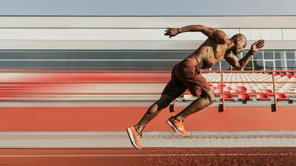 Side view shot of male sprinter running on the sport track. Athlete runner doing workout at the...
