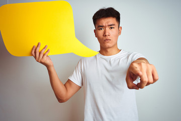 Asian chinese man holding speech bubble standing over isolated white background pointing with...