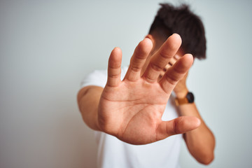 Young asian chinese man wearing t-shirt standing over isolated white background covering eyes with hands and doing stop gesture with sad and fear expression. Embarrassed and negative concept.