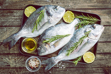 Fresh raw Dorado or sea bream with spices, herbs, lemon and salt over wooden background Top view