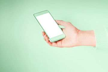 Woman's hand with mobile phone screen on pastel green. Neo mint green color of 2020.