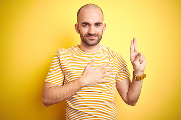 Young bald man with beard wearing casual striped t-shirt over yellow isolated background smiling...