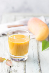 Tropical Mango smoothie in a glass and fresh mango on a light background. Mango shake. Tropical fruit concept.