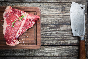 Raw T-bone Steak with fresh herbs and oil on dark wooden background, top view