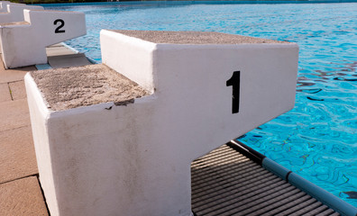 Startblöcke am Beckenrand von einem Schwimmbad. Die Blöcke tragen die Nummer eins, zwei. Die...