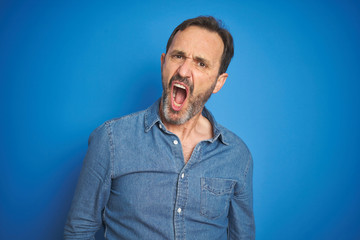 Handsome middle age senior man with grey hair over isolated blue background In shock face, looking skeptical and sarcastic, surprised with open mouth