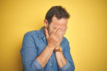 Handsome middle age senior man with grey hair over isolated yellow background with sad expression covering face with hands while crying. Depression concept.