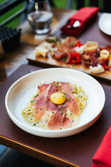 Fettuccine Carbonara with parma ham and yolk with black pepper. Served in white plate with Cold Cuts.