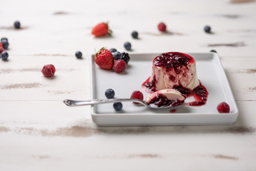 Delicious italian dessert panna cotta with berry sauce, fresh berries on white wooden background
