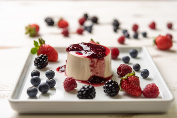 Delicious italian dessert panna cotta with berry sauce, fresh berries on white wooden background