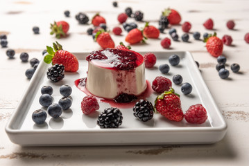 Delicious italian dessert panna cotta with berry sauce, fresh berries on white wooden background