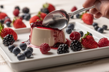 Delicious italian dessert panna cotta with berry sauce, fresh berries on white wooden background