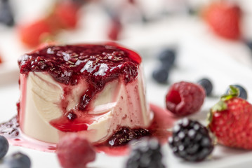 Delicious italian dessert panna cotta with berry sauce, fresh berries on white wooden background