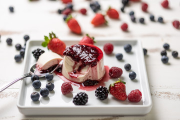 Delicious italian dessert panna cotta with berry sauce, fresh berries on white wooden background