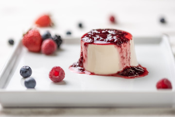 Delicious italian dessert panna cotta with berry sauce, fresh berries on white wooden background