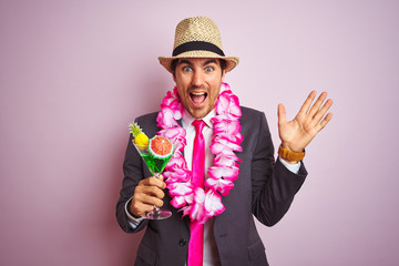 Businessman wearing suit hat hawaiian lei drinking cocktail over isolated pink background very...