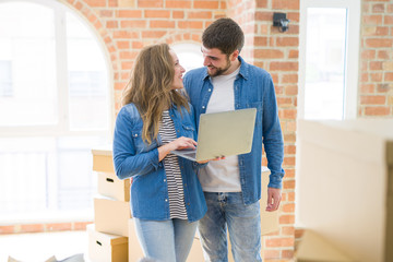 Young couple using computer laptop standing on a room around cardboard boxes, happy for moving to a new apartment