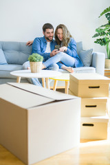 Fototapeta na wymiar Young couple in love hugging sitting on the sofa using smartphone very happy moving to a new home