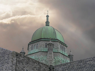 Fototapeta na wymiar Dome of Galway Cathedral with cross on a bright cloudy sky and ray of light going, Concept religion, hope.
