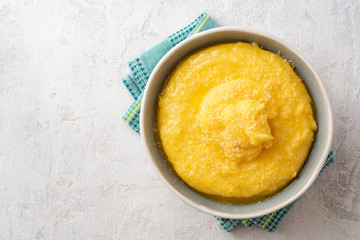 Polenta with butter and parmesan cheese in bowl on concrete background. Top view. Copy space.