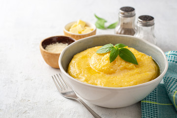 Polenta with butter and parmesan cheese in bowl on concrete background. Selective focus.
