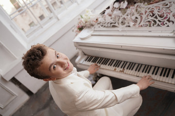 young man teenager in a white business suit with a large white piano in flowers. caucasian male...